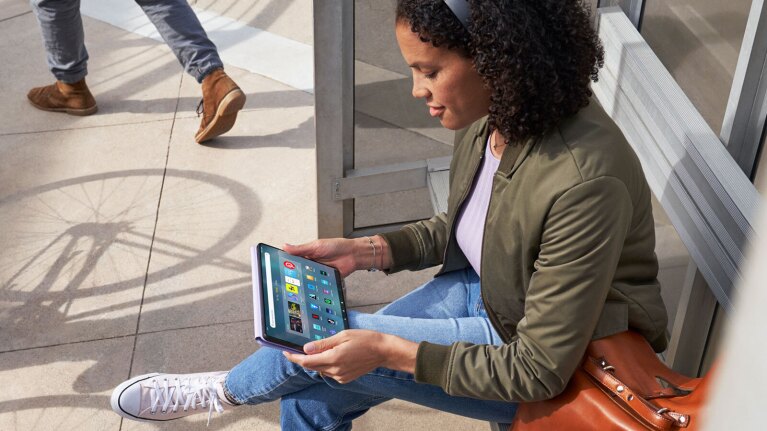 An image of a woman sitting by a bus stop using Amazon's Fire Max 11 tablet.