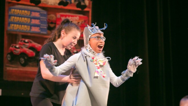 一位身着传统服装的舞者执行与一个辅助的支持。舞台装饰在后台显示玩具和游戏。