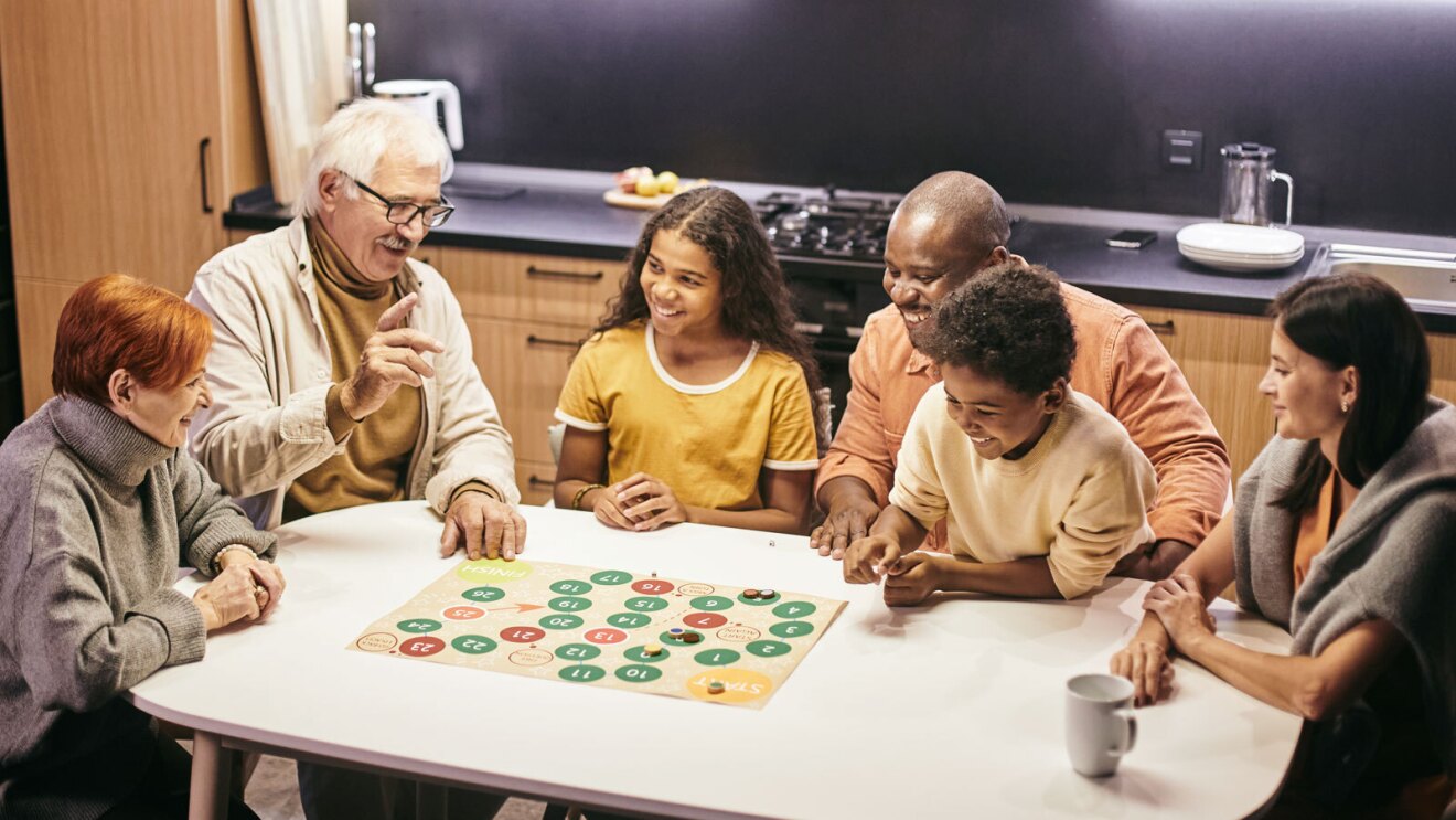 Two children and four adults sit around a table smiling as they play a game.