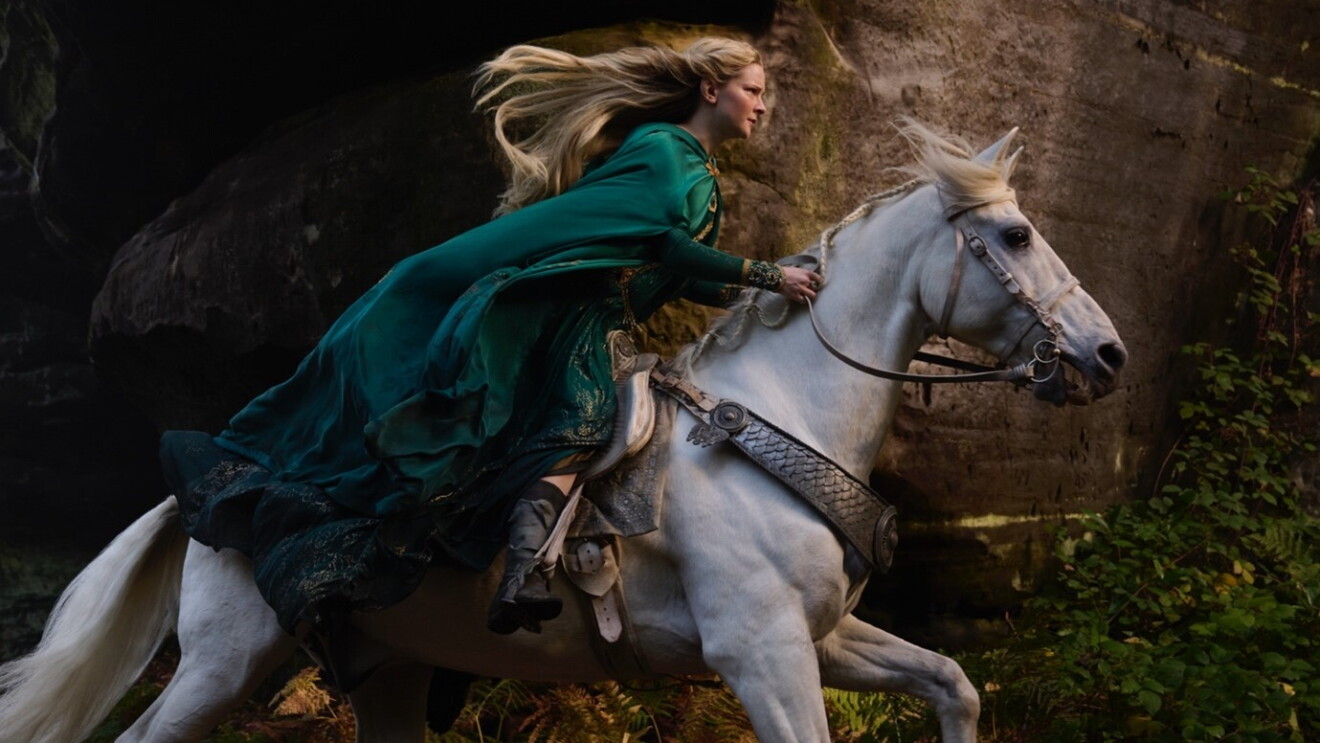 A blonde woman wearing a green cloak on a white horse