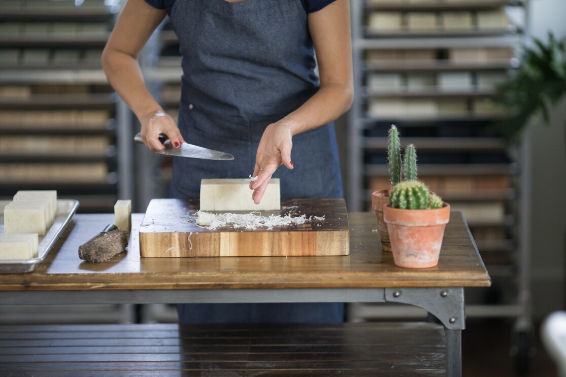 An employee at Little Flower Soap Company cuts a block of soap by hand, to create bars of soap to be packaged and shipped to customers.