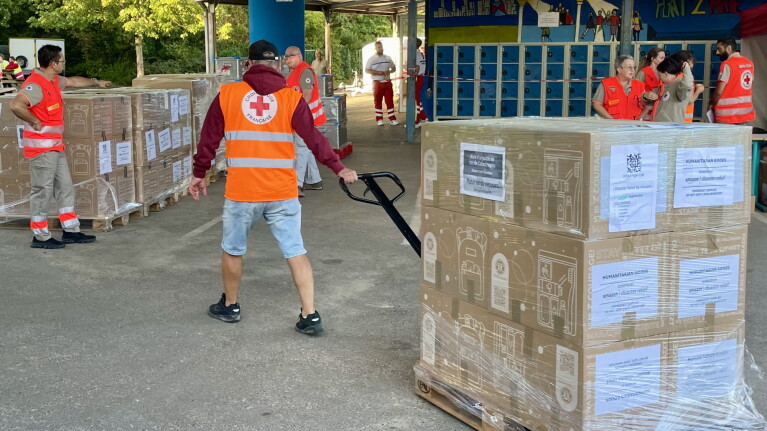Red Cross volunteers moving pallets of humanitarian aid supplies in a warehouse