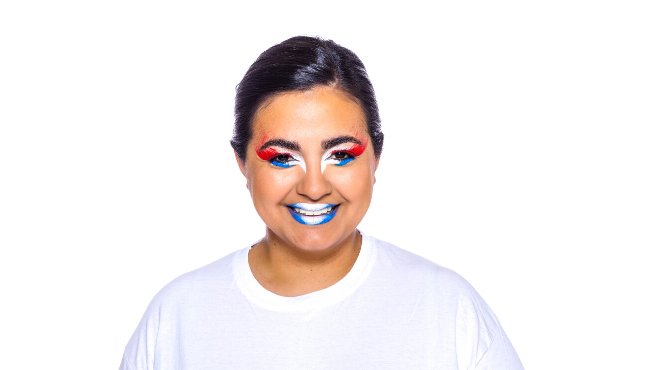 Para el Día de la diversida Amazon ha preparado una acción con asociados de diferentes países que llevan la bandera pitnada en su cara. En la foto, Íngrid con camiseta blanca, mirando sonriendo a cámara con la bandera de su país puntada en la cara. Tiene el pelo negro oscuro rcogido con una coleta detrás. 