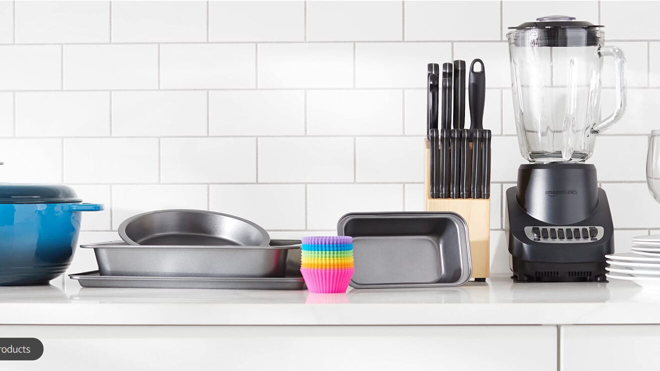 An assortment of kitchen supplies, dutch oven, baking pans, muffin liners, blender, and plates, on a kitchen countertop 