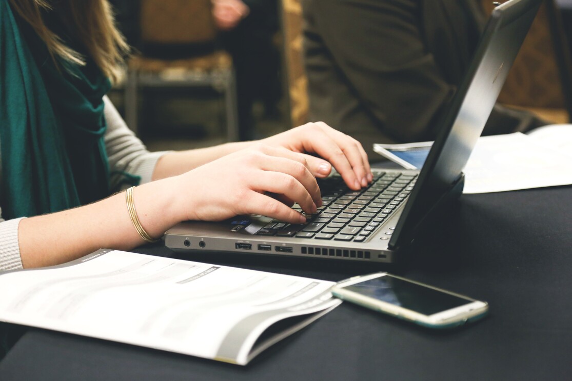 Woman working on a laptop computer, her hands are posed over the keyboard of the device. 