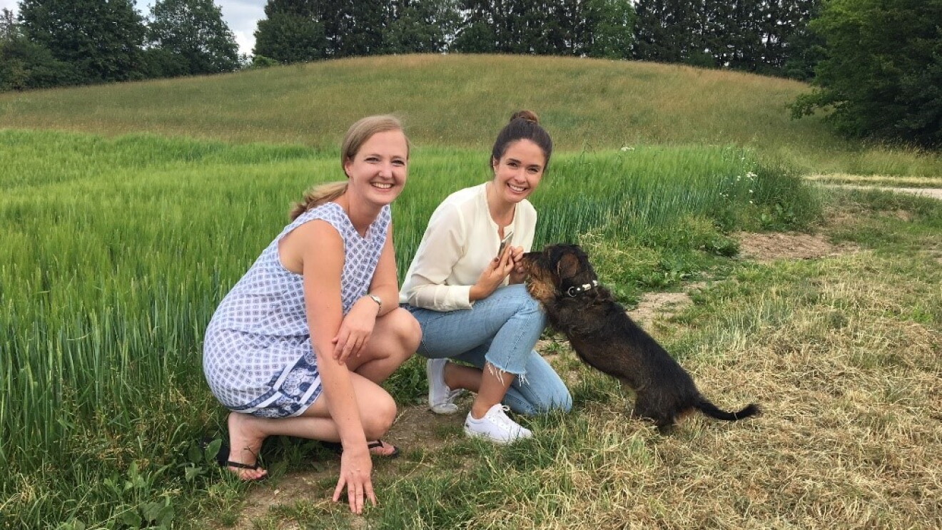Die Gründerinnen von kleine PHARM und Varia Living sitzen auf einem abgemähten Getreidefeld und spielen mit einem Dackel. Sie lachen in die Kamera.