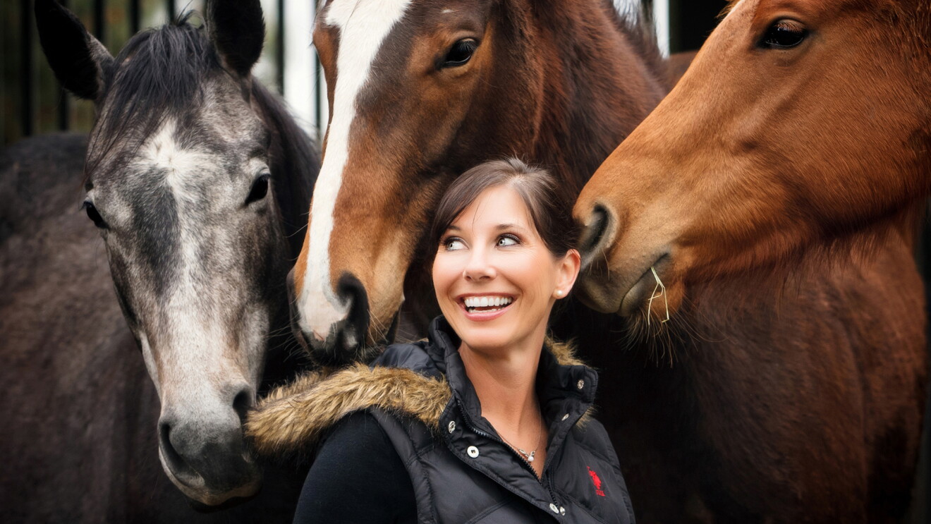 A smiling woman looks back over her shoulder. Three horses surround her.