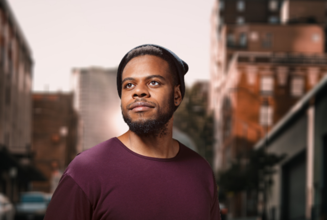 An image of a man looking off into the distance for a headshot. Behind him is a city landscape.