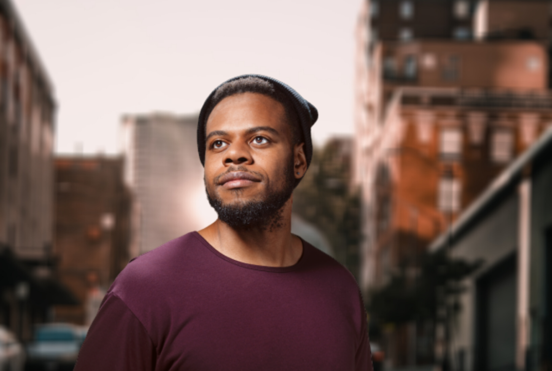 An image of a man looking off into the distance for a headshot. Behind him is a city landscape. 