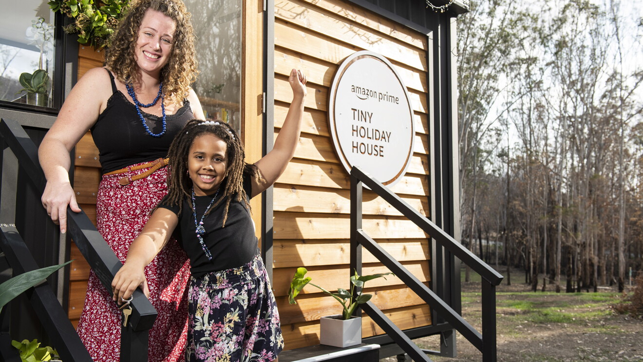 A woman and her child stand on the front steps of a tiny house