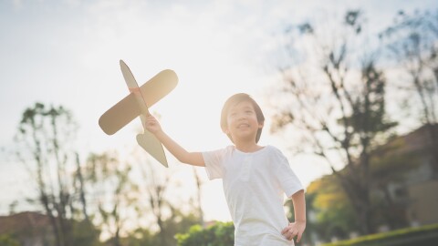 Boy running and holding a cardboard plane, making it fly