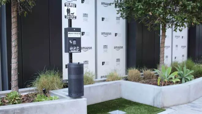 屋外のスペースの一部に人工芝がひかれていて、ゴミ箱などが置かれている。その横に人と犬を描いた標識がある