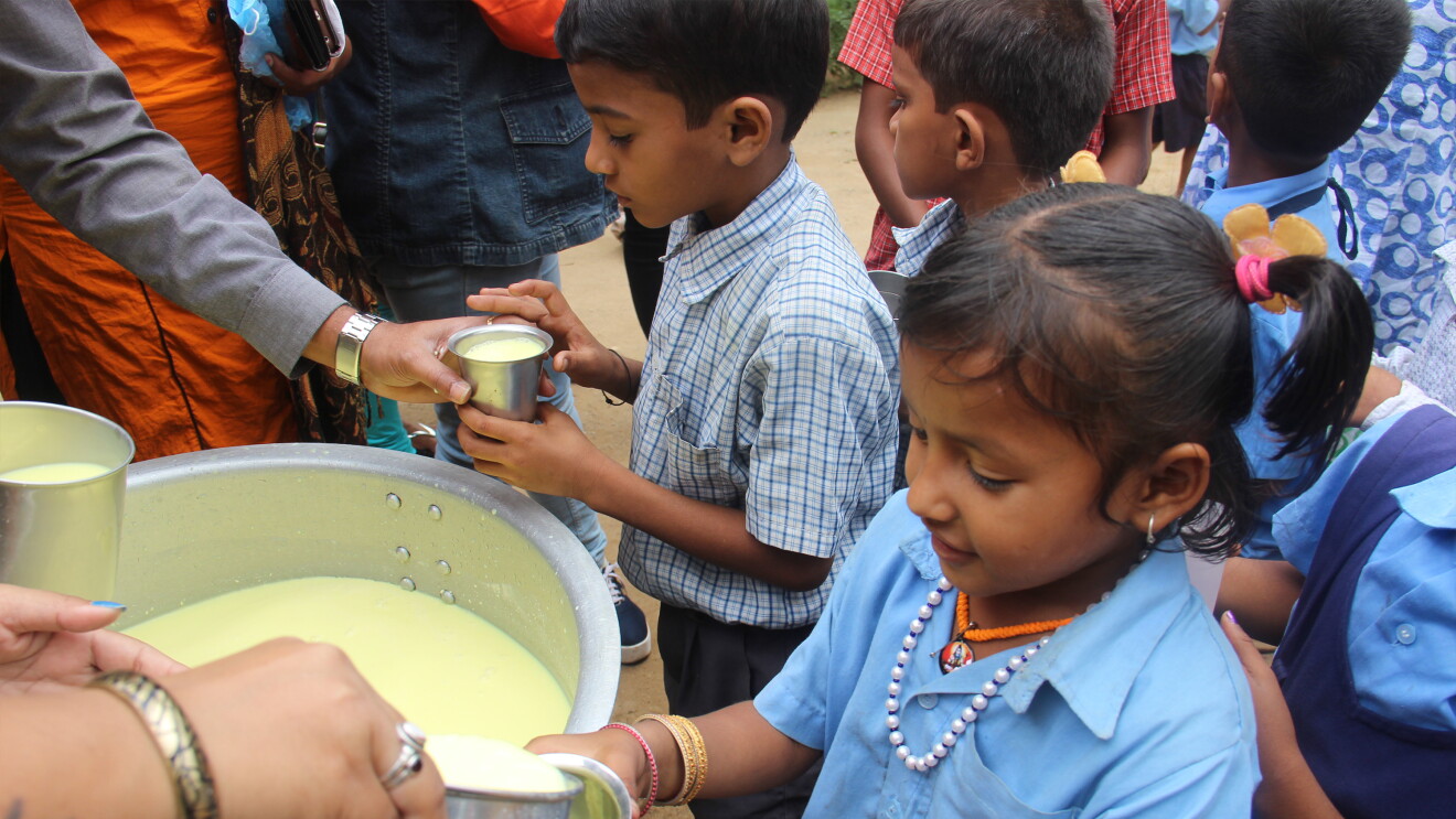 A school girl from a government school getting his glass of milk, even as the boy behind him in the queue looks on