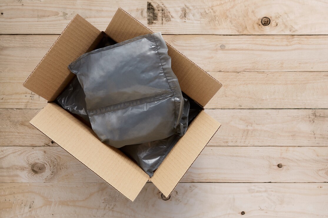 Sobre un fondo de madera aparece una cajas rectangular de Amazon con dos almohadillas de plástico de color gris.