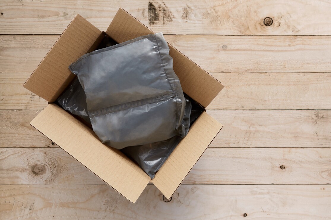 Sobre un fondo de madera aparece una cajas rectangular  de Amazon con dos almohadillas de plástico de color gris. 