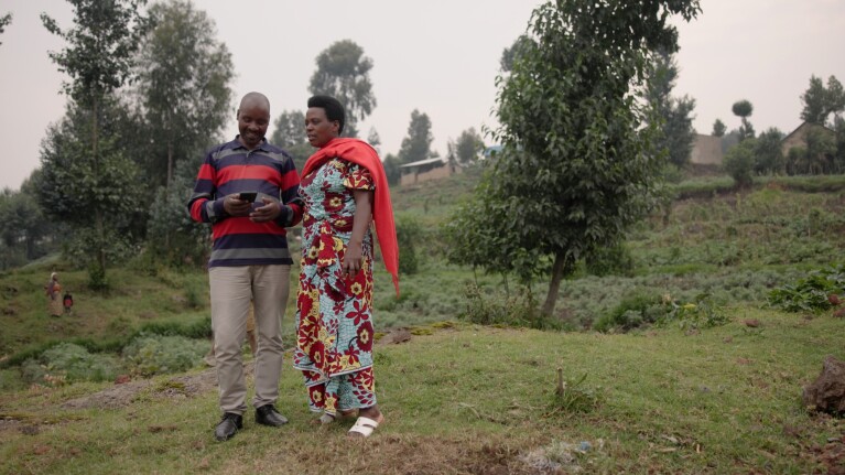 A couple stood in a rural hillside setting looking at a mobile phone