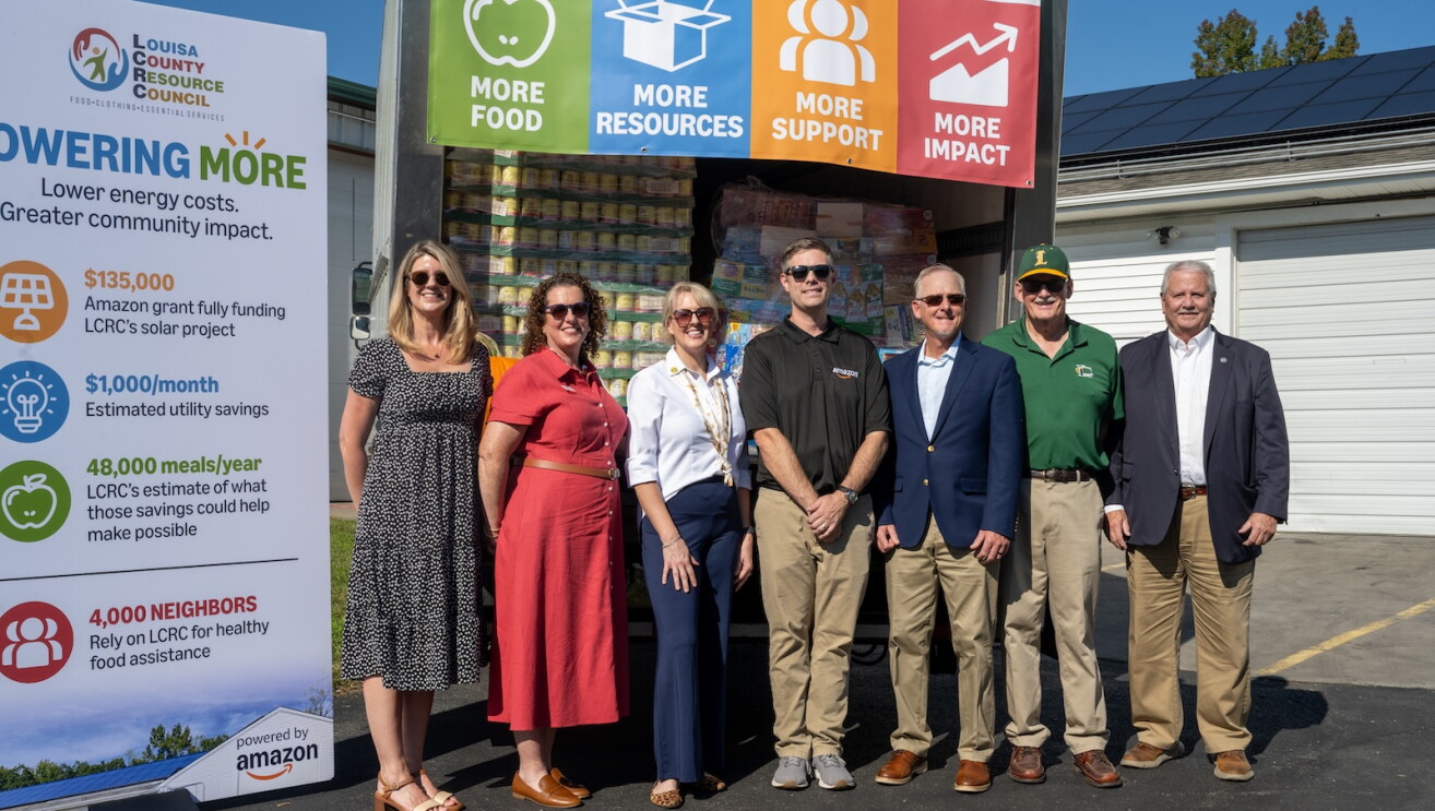 Community leaders and Amazon representatives stand in front of a banner alongside a supply truck delivering goods for the Louisa County Resource Council in Virginia.