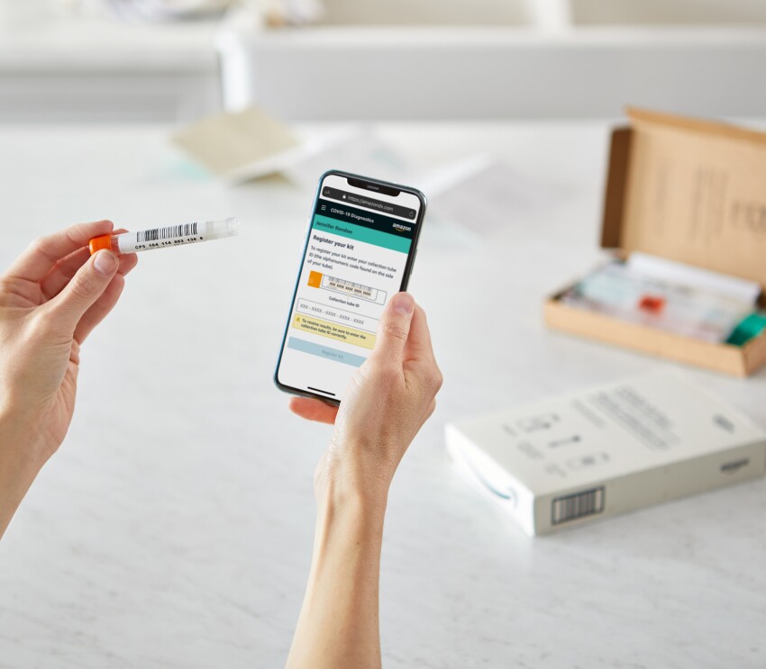 An image of the Amazon COVID test being used alongside the iPhone. A person is holding the test tube next to a mobile phone displaying a screen with a prompt to register the kit.