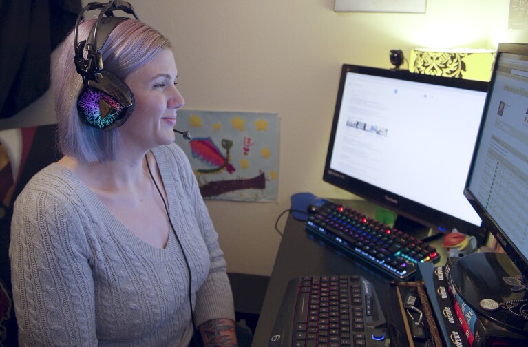A woman wears a headset while looking at two computer monitors.