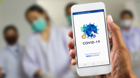 World Health Organization Academy app on a mobile phone, held in a patient's hand with four medical personnel blurred out in the background. 