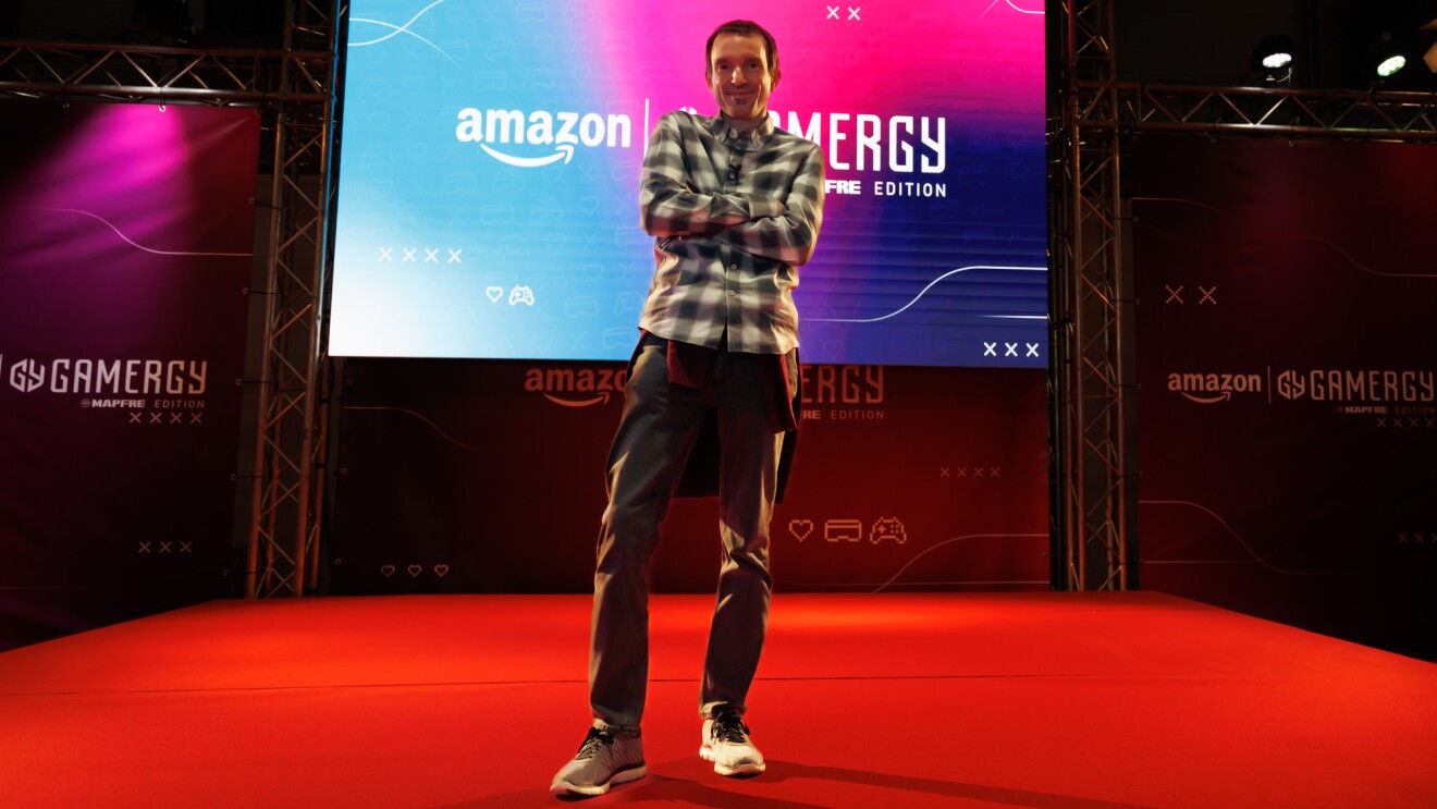 Eduardo García, responsable de Gaming y esports de Amazon Retail Europa. Eduardo con el pelo corto negro y mascarilla quirúrgica jugando a videjojuegos. Lleva una camisa de cuadros grises, negros y blancos.