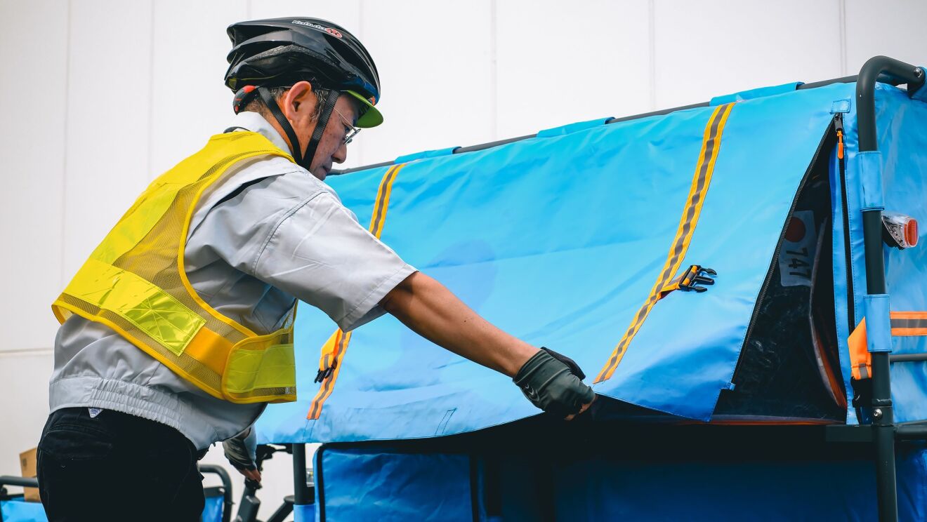 ヘルメットを被っている男性がリアカーの青いカバーを閉じている。その中には大きな荷物が見える