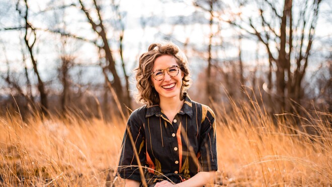 亚马逊音乐艺术家负责人Katie (schlosser) vitolins的专业形象。她坐在田野里微笑着拍照片。