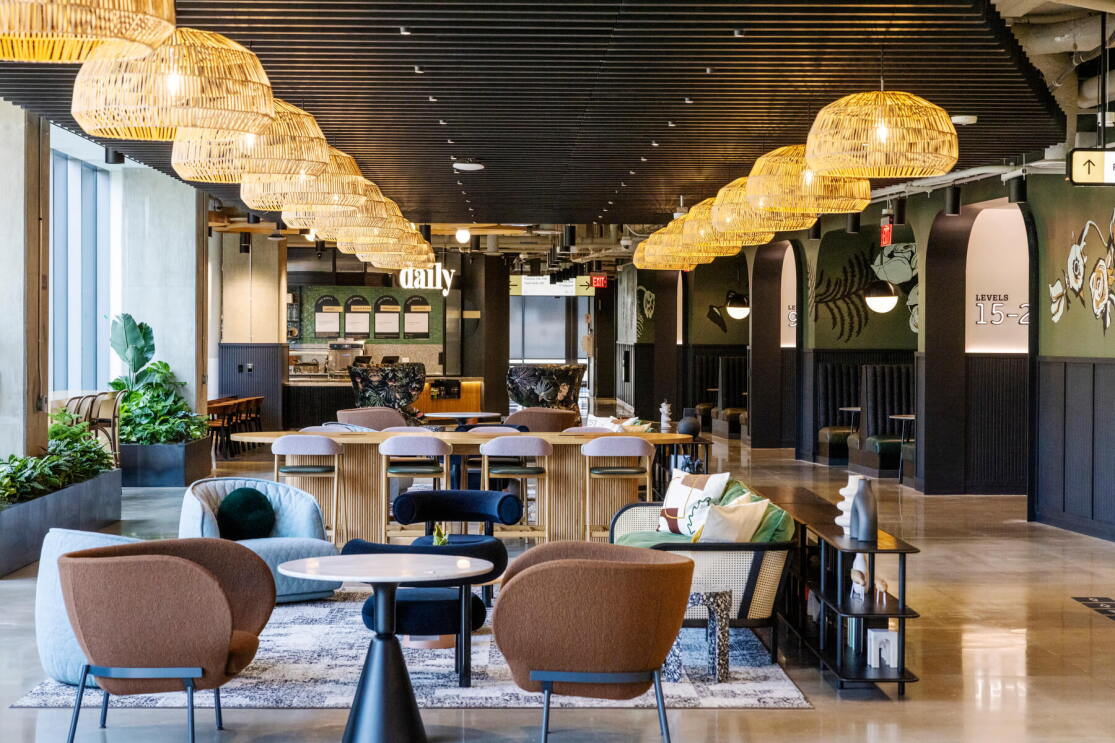 An image of a dining area at Amazon HQ2. There are several tables and chairs and beautiful light fixtures made of light whicker. 