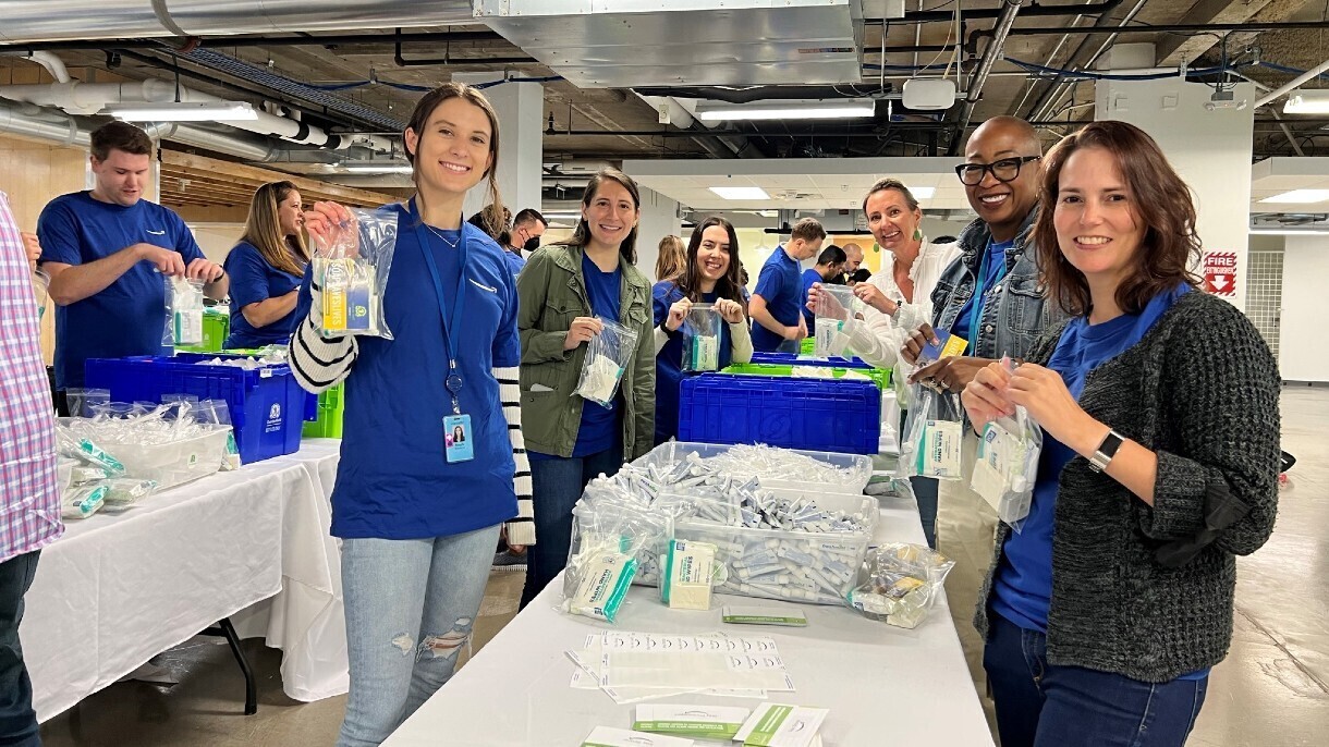Amazon employees wear blue Amazon T-shirts and hold up the hygiene kits they are packing.