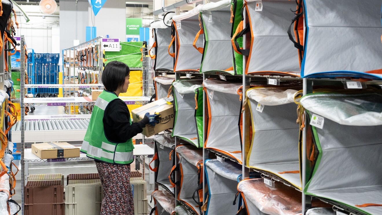 箱型の入れ物に商品の入った段ボール箱を入れている女性