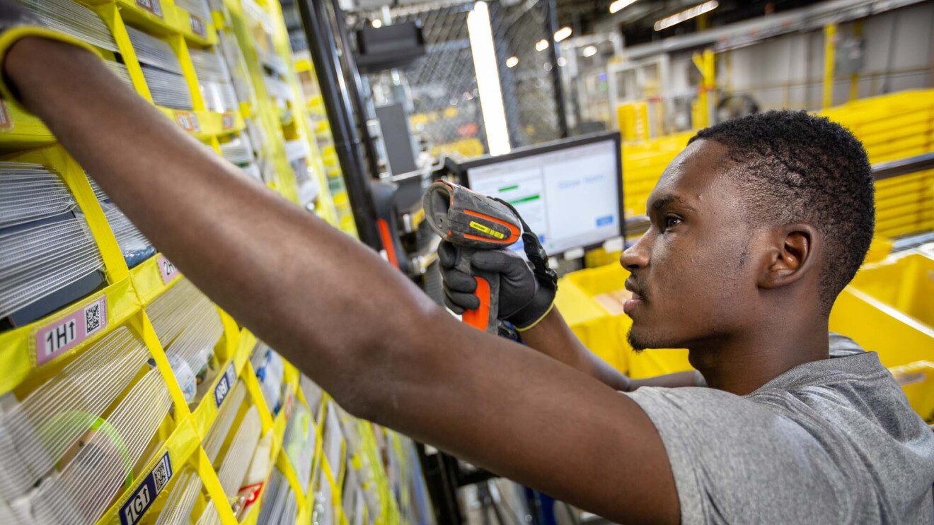 An Amazon associate holds a scanner in his left hand while reaching for a customer's product, at a Columbus, Ohio fulfillment center, CMH1