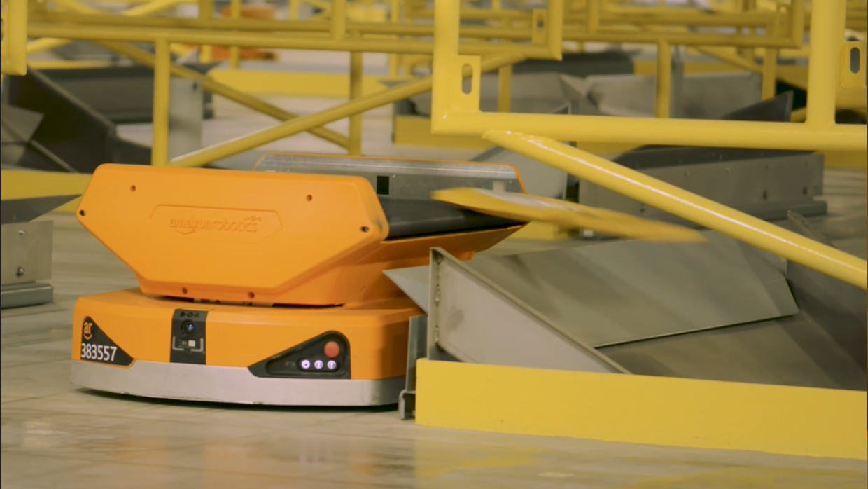 Los Pegasus Drives reciben los paquetes individualmente en su cinta transportadora, se mueven a través del campo robotizado y los colocan en la rampa. Foto lateral del drive, de color naranja, que lanza el paquete a la rampa. 