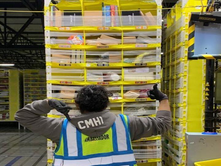 A woman working at an Amazon fulfillment center points at the hood of her sweatshirt, while stowing items.