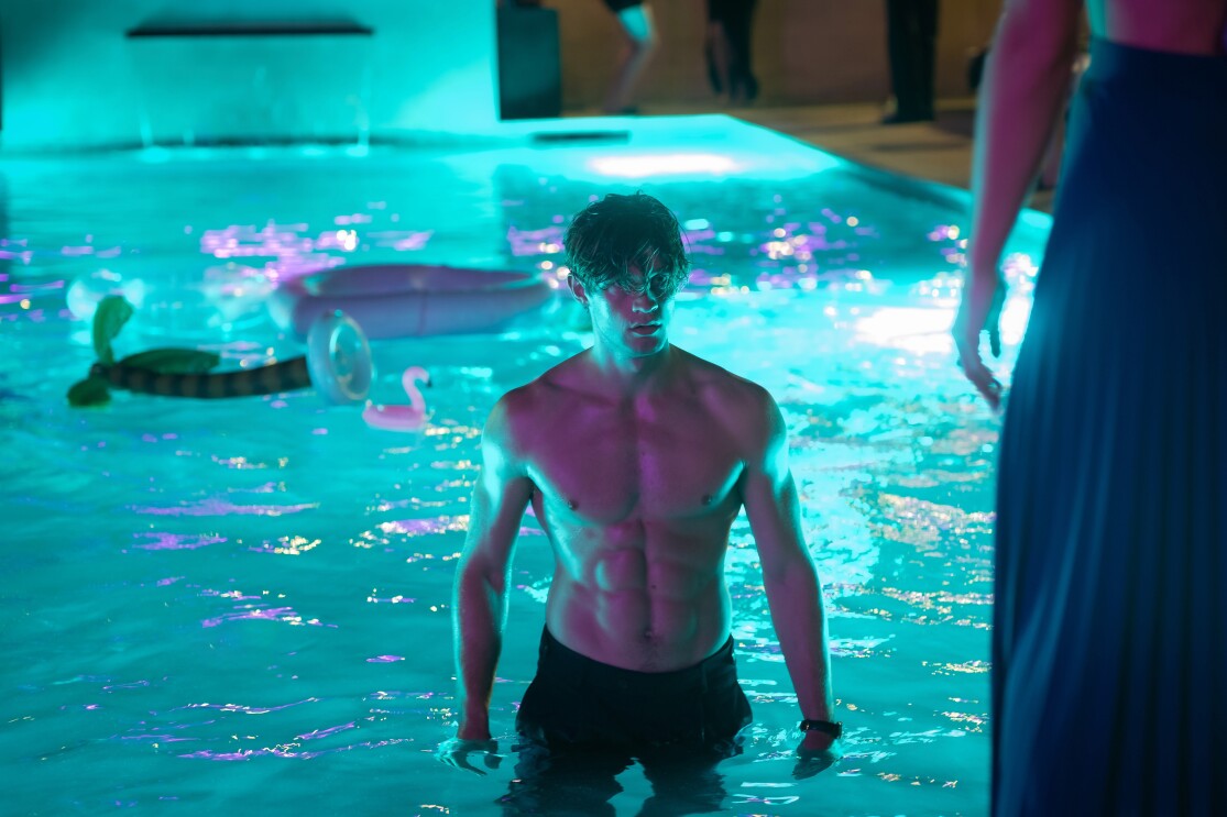 James Beaufort ohne Hemd steht in einem beleuchteten Pool bei einer Nachtparty