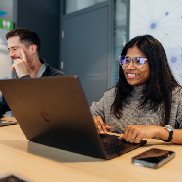 An man and woman sitting at a table in a modern collaborative workspace working on their laptops side by side, smiling