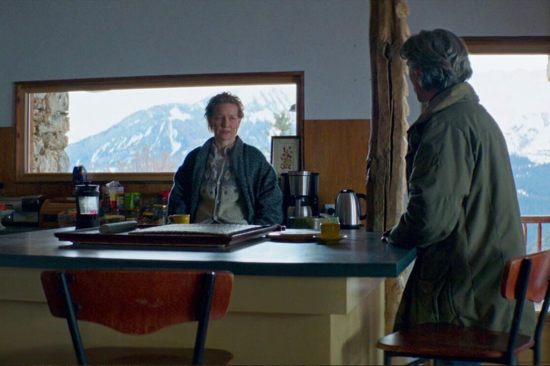 A man and a woman stand in a kitchen with the french alps in the background