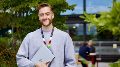 Smiling person holding HP laptop outdoors with rainbow lanyard
