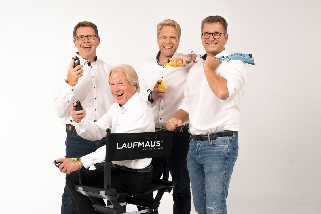 Vier Männer in weißen Hemden halten Laufmäuse in den Händen und lachen in die Kamera.