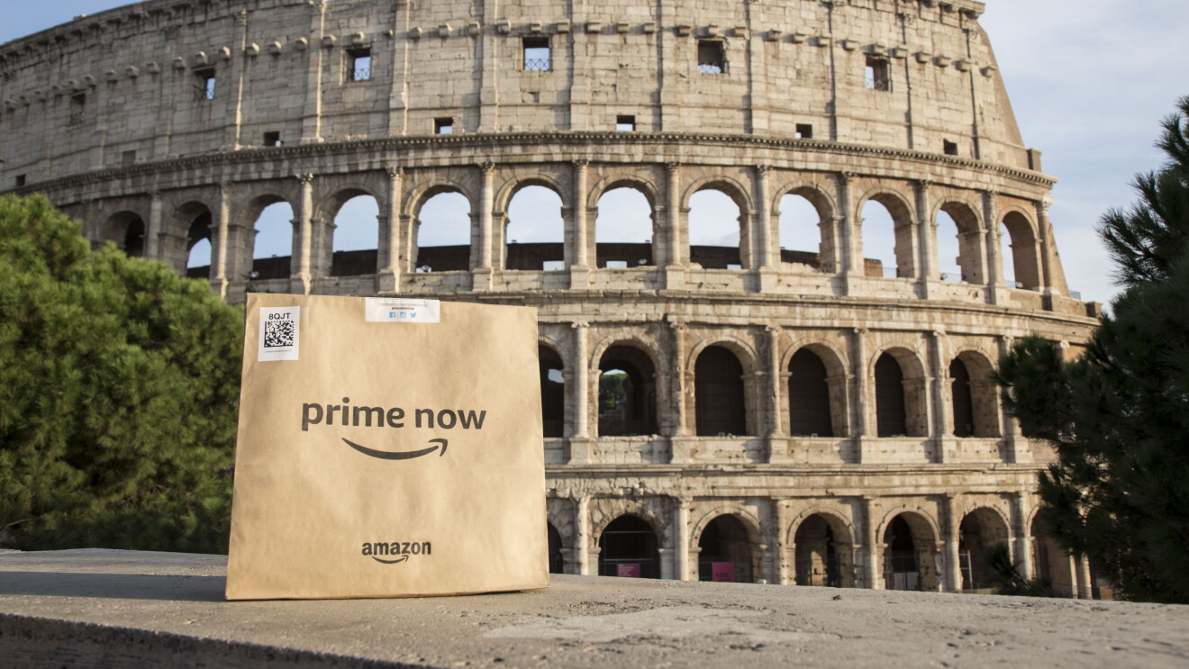 Package with Amazon and Prime Now logo on the front sits across the Colosseum  in Rome. 