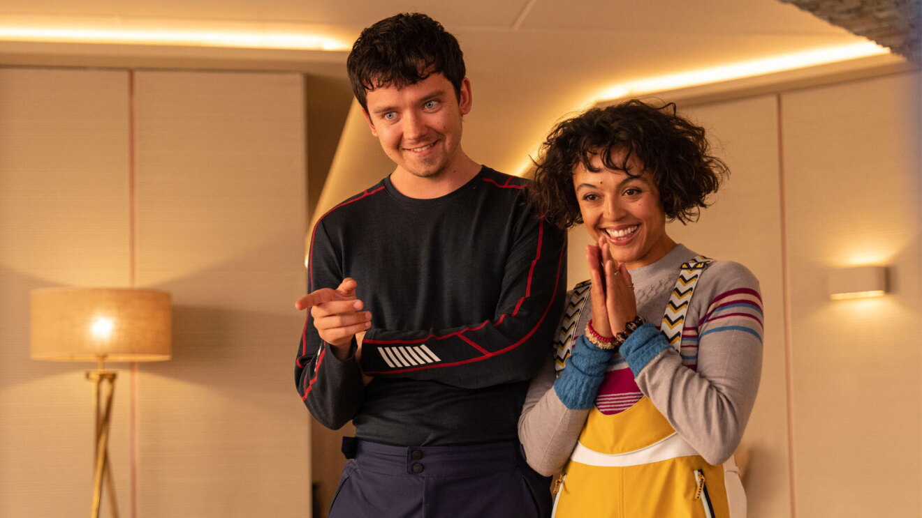 An image of a man and a woman standing beside each other. They are smiling and looking at something behind the camera.