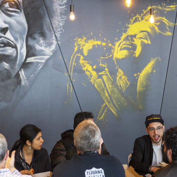 Amazon employees hang out  in front of a grey wall with murals of famous musical artists.