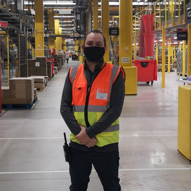 Liam Fletcher, WHS Coordinator at Amazon's fulfilment centre in Warrington, pictured wearing a high visibility vest and face mask.
