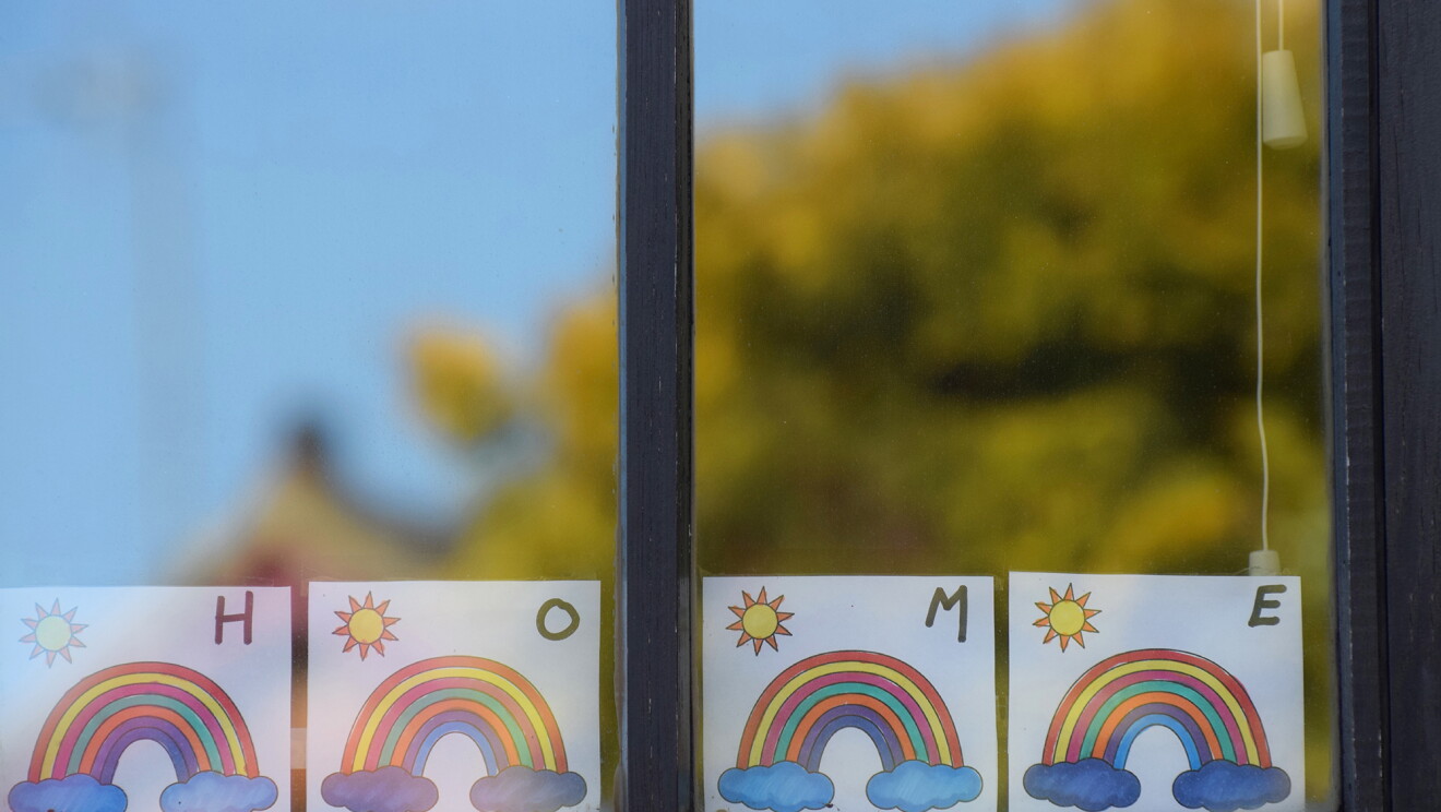 A child placing homemade rainbows in the window of their home, during COVID-19 pandemic.