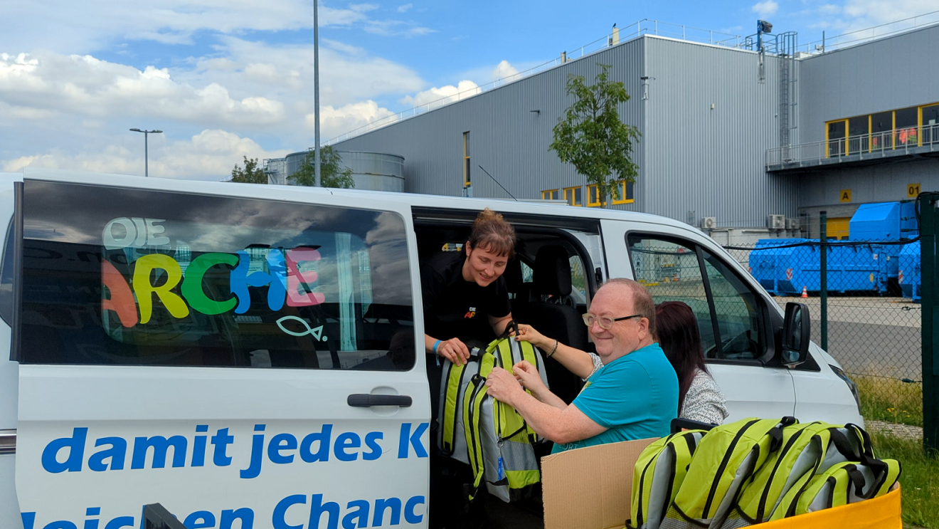 Amazon Mitarbeiter und Mitarbeiterin in Leipzig laden bunte Back to School Rucksäcke in einen Minibus von Die Arche ein