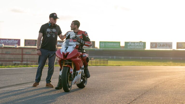Motorcyclist on racing bike consulting with coach on race track.