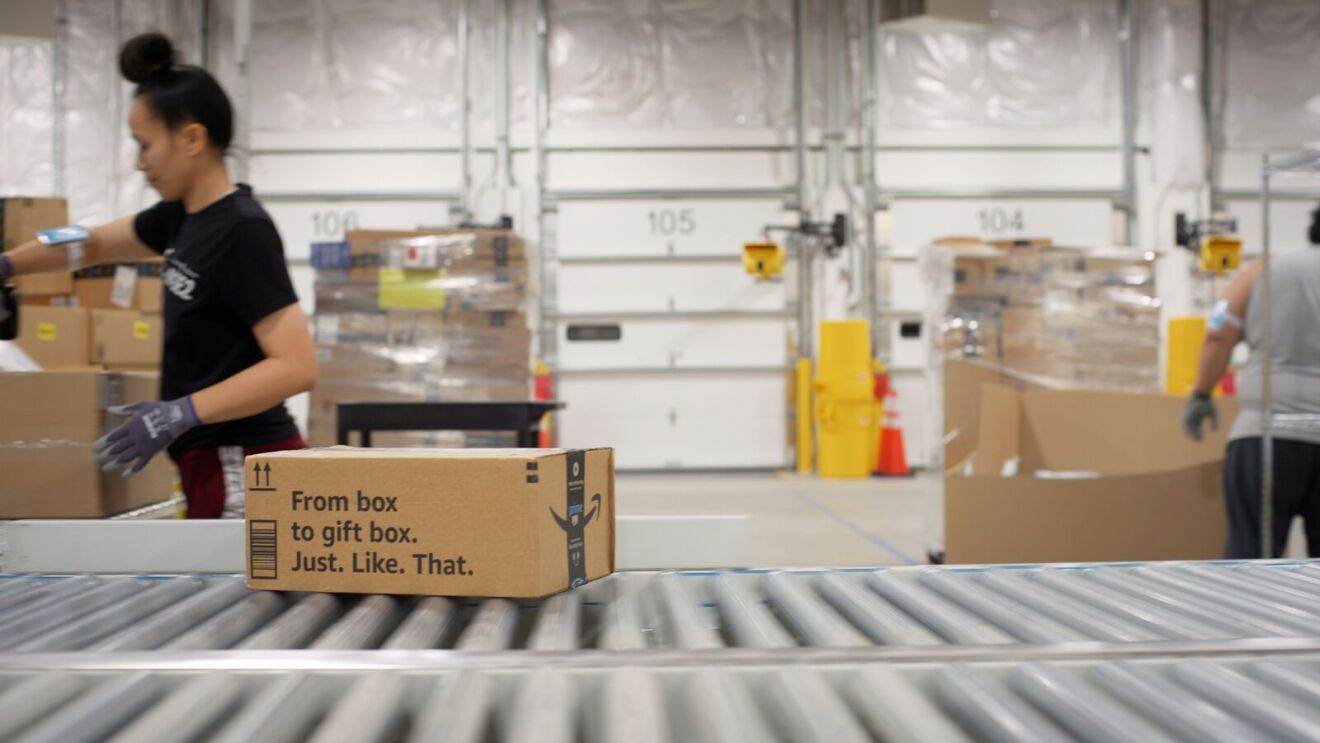 Amazon fulfillment employee processing packages on conveyor belt.