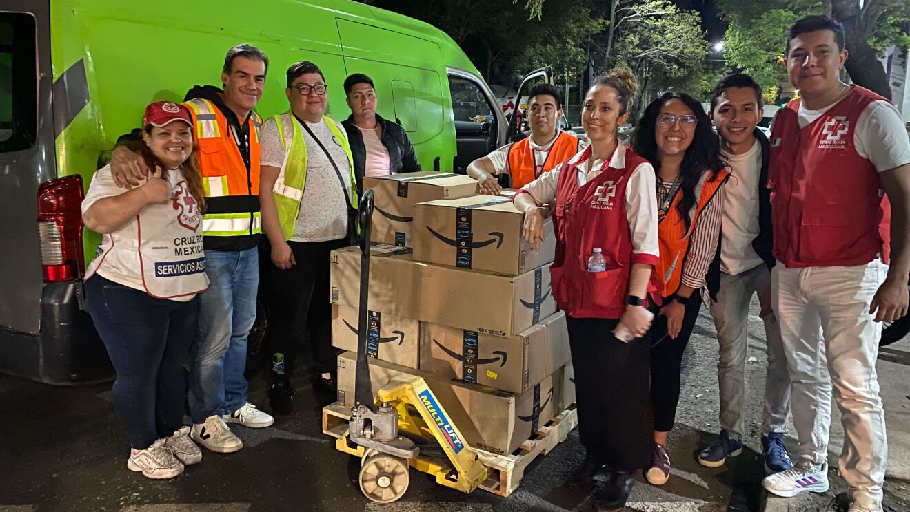 Nueve personas delante deun palé con cajas de Amazon delante de una furgoneta azul.