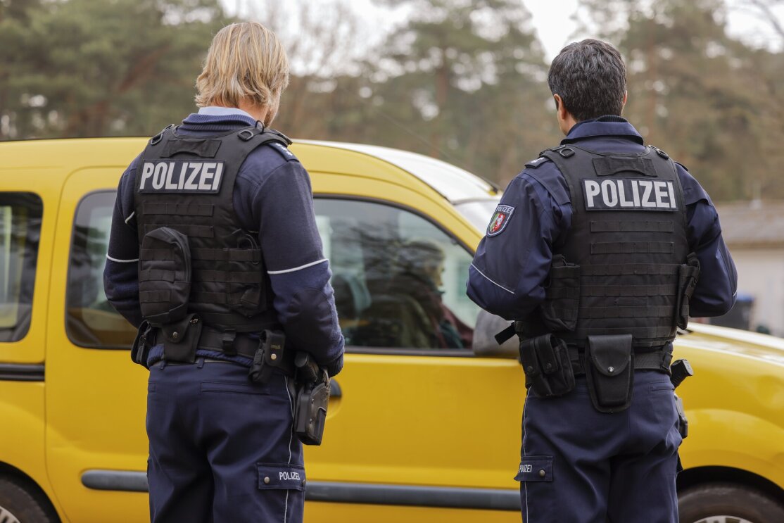 Zwei deutsche Polizeibeamte stehen neben einem gelben Fahrzeug.