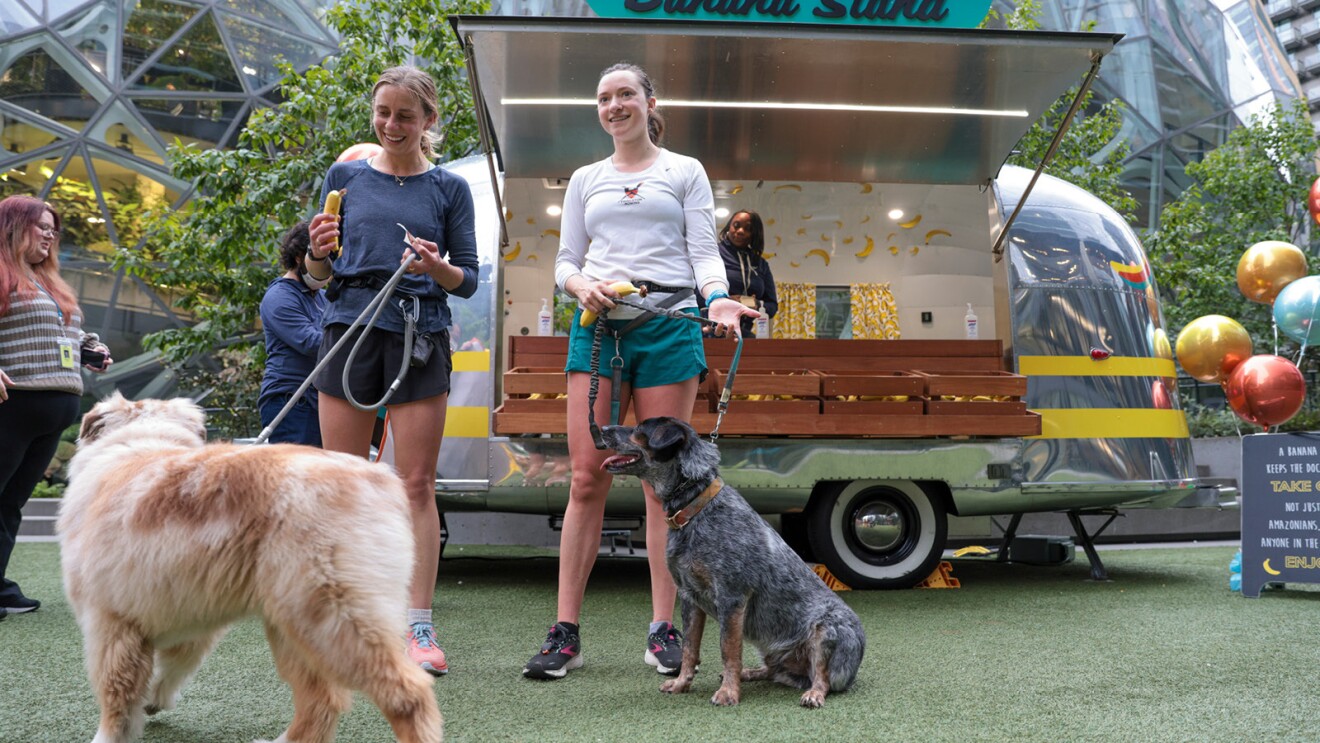 Two women and their dogs standing in front of Amazon's banana stand in front of the Spheres in Seattle.