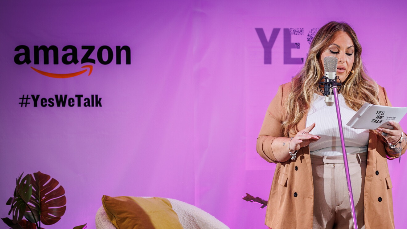 En un escenario creado para la ocasión, de fondo hay un cartel con el logo de Amazon, el Yes, we talk, que es el lema de la campaña y el lema de la sesión Rompiendo el silencio. Todo el fondo es de color rosa. En el escenario, 6 plantes con sus respectivas macetas, dos mesas y dos sillas. Nicole, una trabajadora de Amazon, está de pie delante de un micro y hablando agarrando con la mano izquierda unos papeles. La directora de cine Leticia Dolera. Nicole va vestida a tonos beis. Con un pantalón acampanado, un jersey y una americana. Lleva el pelo largo, ondulado, castaño con mechas rubias, Leticia Dolera va con una americana gris, jersey negro de lana de cuello alto, pantalón negro y botines animal print. Es pelirroja, lleva el pelo largo hasta el pecho y todo a un lado. Leticia está mirando a Nicole.